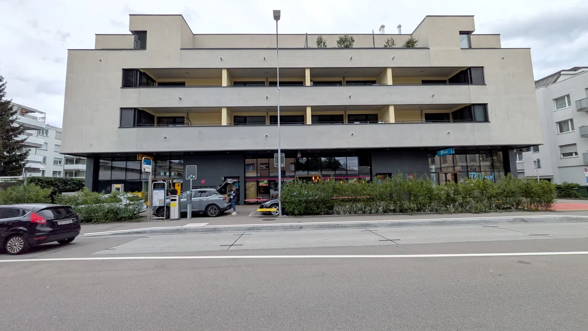 Blick auf die Post Dübendorf mit Strasse und Parkplätzen.